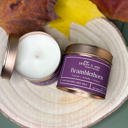 Candle in a tin with a purple label on a surface with autumn leaves