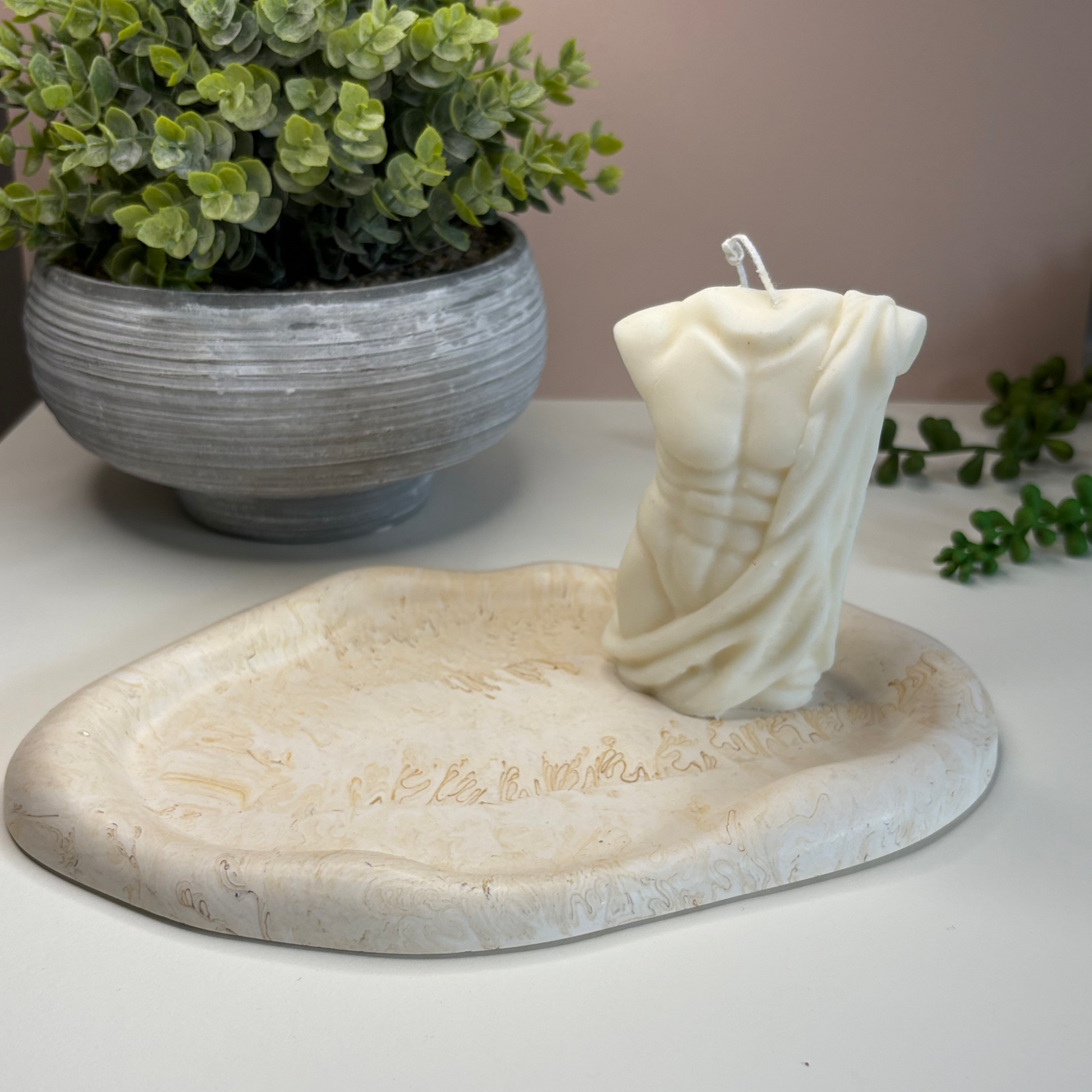 Eco-friendly stoneware candle holder with a plant in the background on a neutral surface.