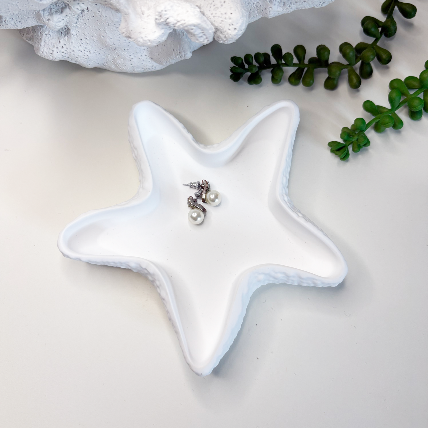 Star-shaped ceramic dish with jewelry on a light background, surrounded by greenery.