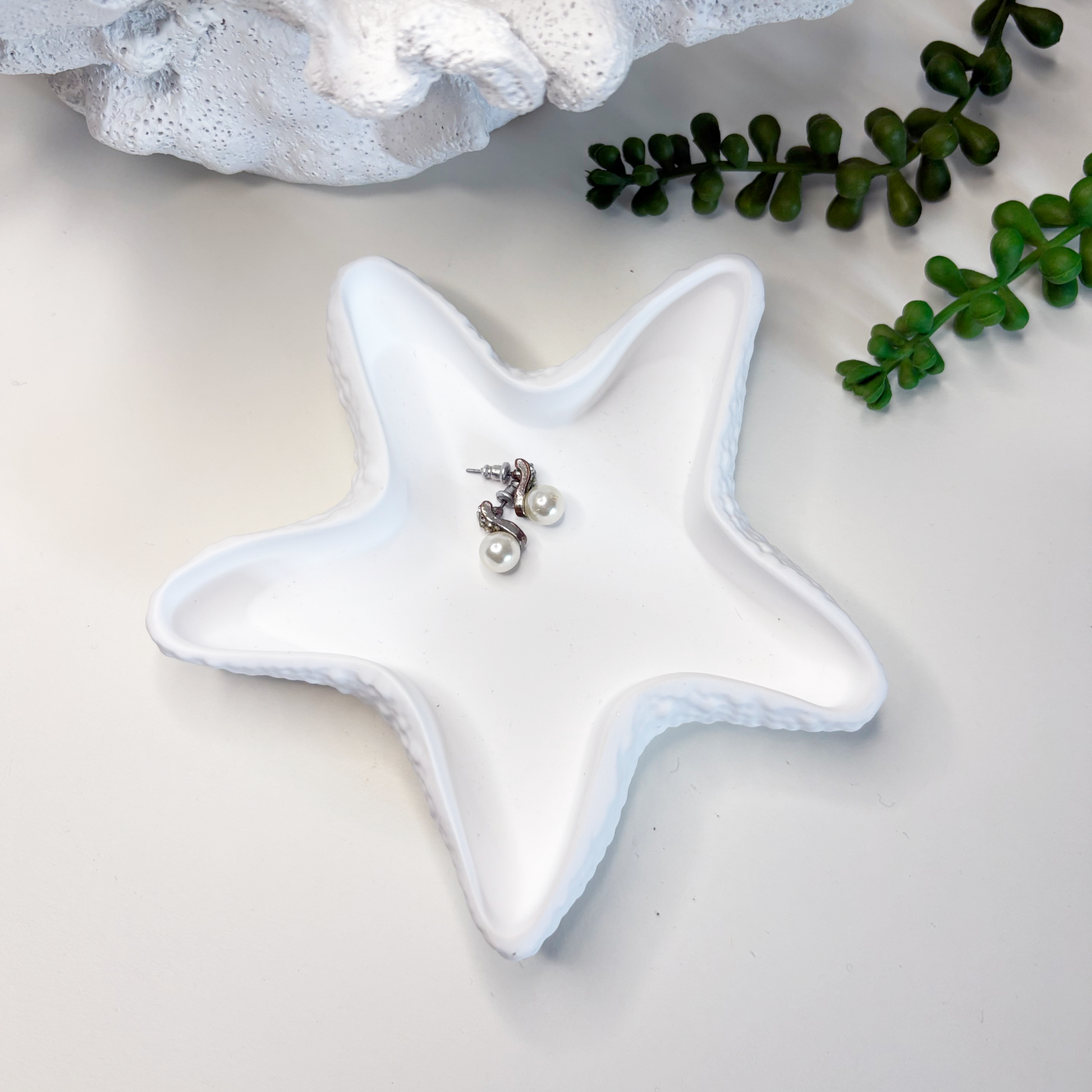 Star-shaped ceramic dish with jewelry on a light background, surrounded by greenery.