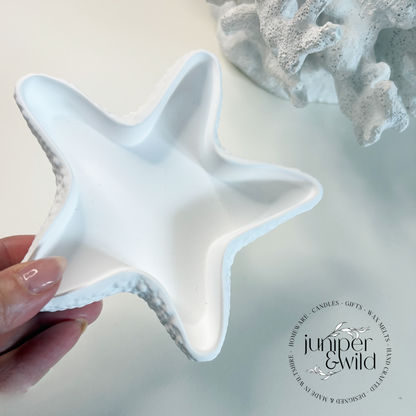 Star-shaped ceramic dish held by a hand with coral decor in the background, branded 'juniper & Wild'.