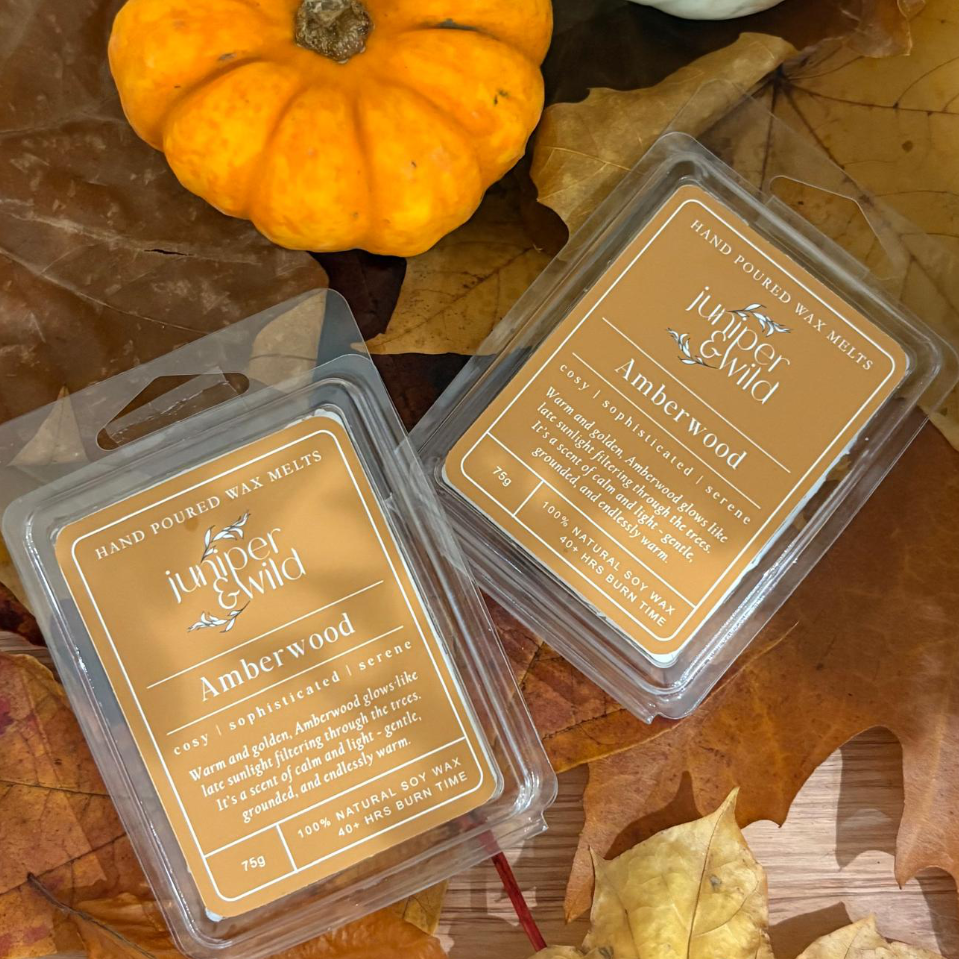 Two packages of Juniper & Wild Amberwood wax melts on autumn leaves with a small pumpkin.