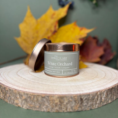 Candle labeled 'White Orchard' on a wooden surface with autumn leaves in the background