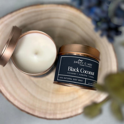 Candle in a tin with a decorative lid on a wooden surface, surrounded by flowers.