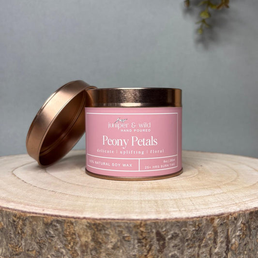 Candle in a pink tin with a bronze lid on a wooden surface against a gray background