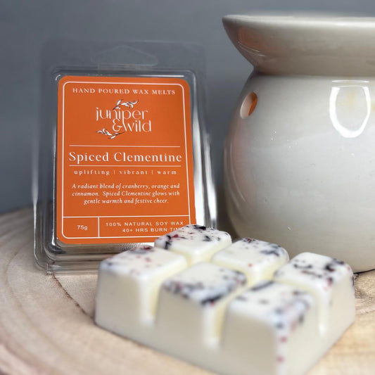 Spiced Clementine wax melts by Juniper & Wild with a ceramic warmer on a wooden surface.
