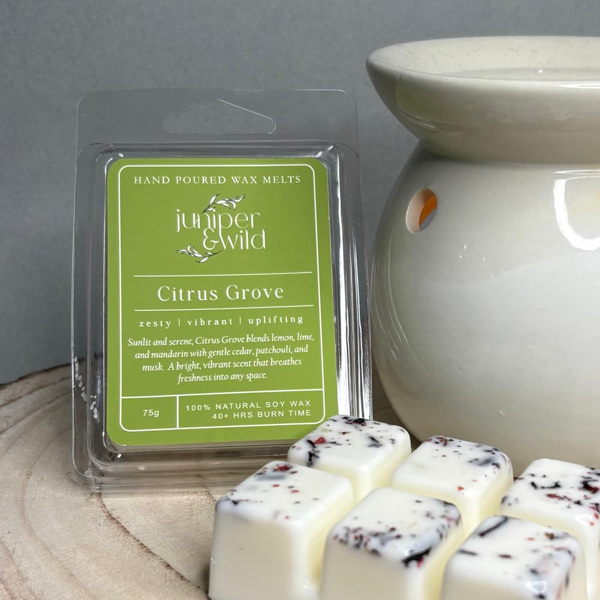Hand poured wax melts with a Juniper & Wild label next to a wax melt warmer on a wooden surface.