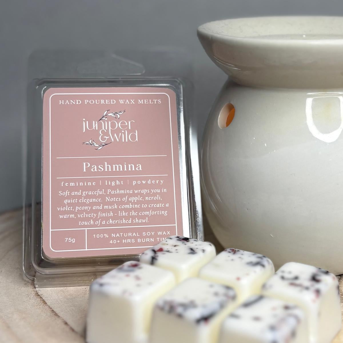 Wax melts in a 'Pashmina' flavor packaging with a ceramic warmer on a wooden surface.