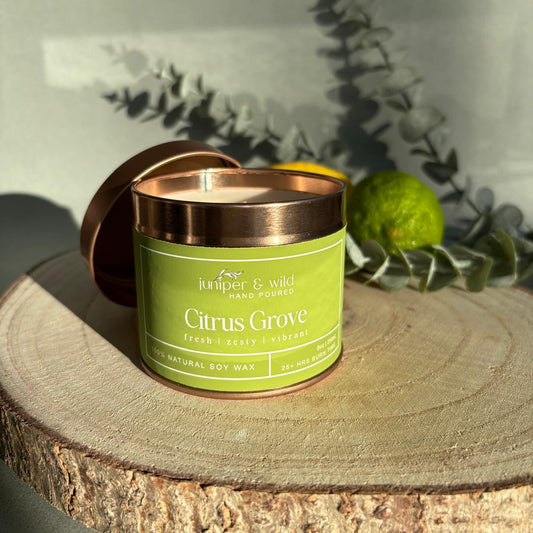 Candle jar labeled 'Citrus Grove' on a wooden surface with greenery in the background