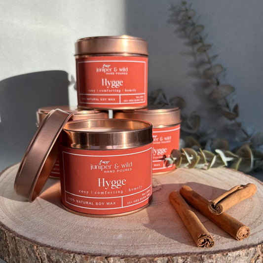 Three 'Juniper & Wild' Hygge candles on a wooden surface with cinnamon sticks.