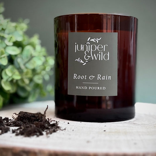 Candle labeled 'juniper & wild' on a wooden surface with greenery in the background