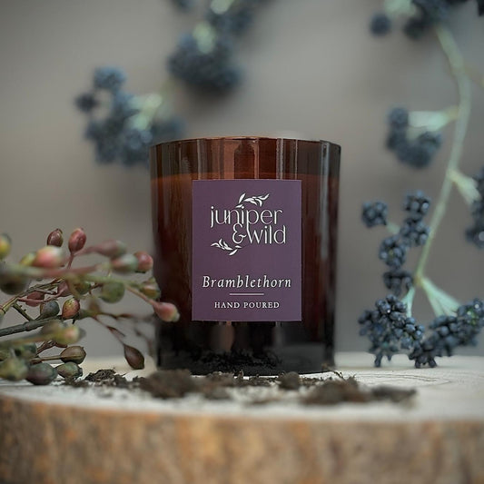 Candle with 'juniper & wild' label on a wooden surface with decorative elements