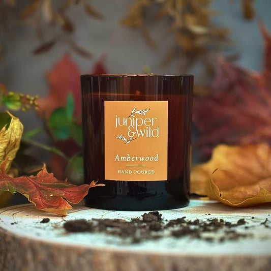 Candle with 'juniper & wild' label on a wooden surface with autumn leaves
