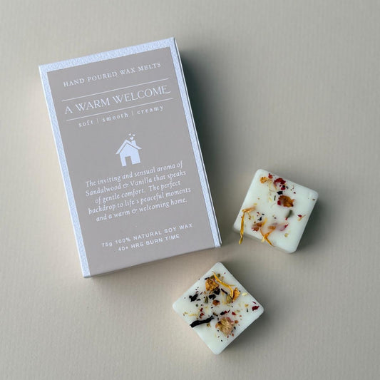 2 botanical wax melt cubes next to a wax melt box with scent called A Warm Welcome from Juniper & Wild